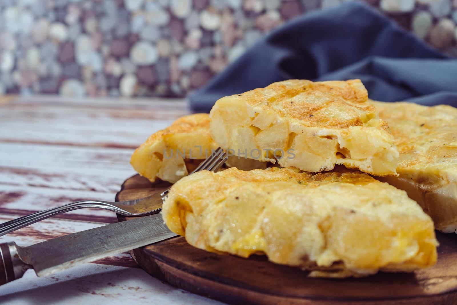 Normal view of a plate with a Spanish potato omelette cut in eighths on a wooden table. Traditional food.