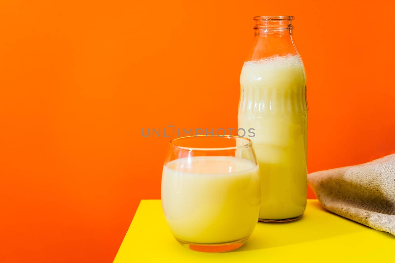 Glass bottle and large glass with milk on a yellow table with orange background. Copy space.