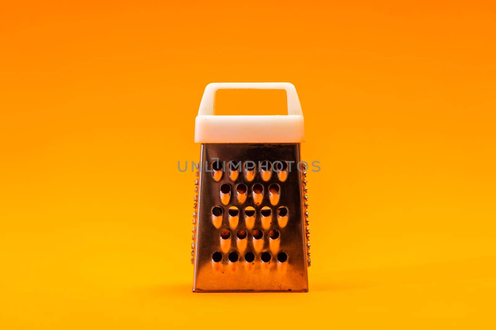 A small shiny metal grater isolated on orange background, close-up of cheese and food stainless grater.