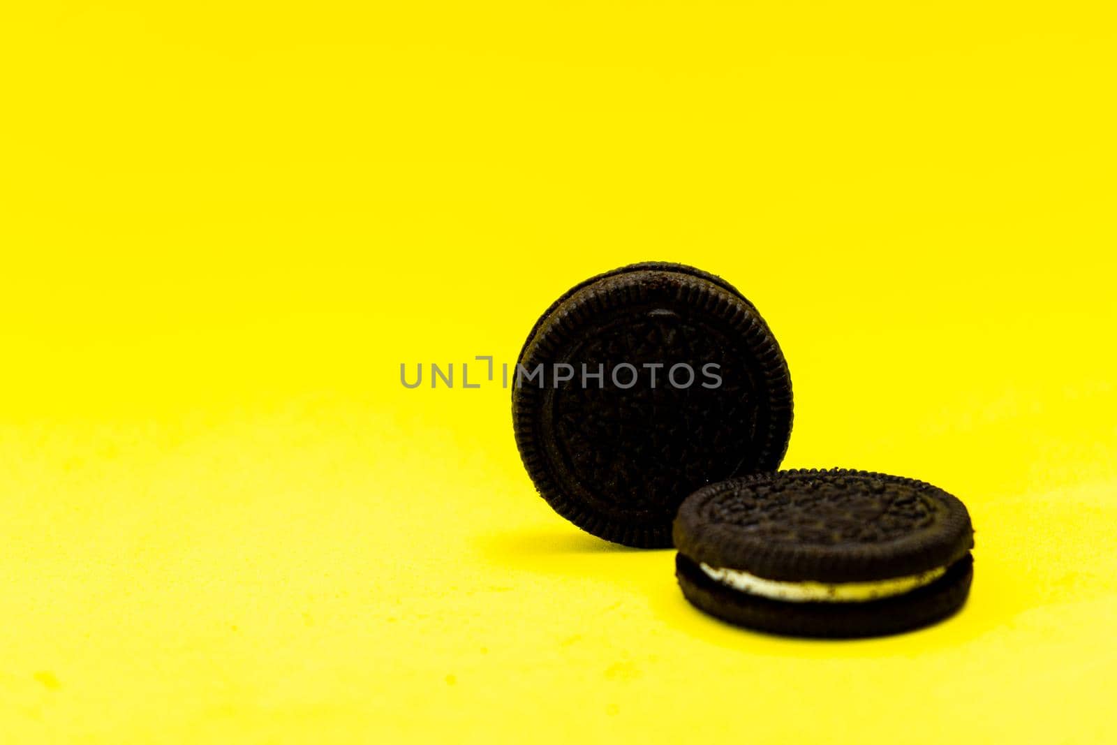 Two chocolate sandwich cookies with sweet cream on a yellow surface. Copy space.