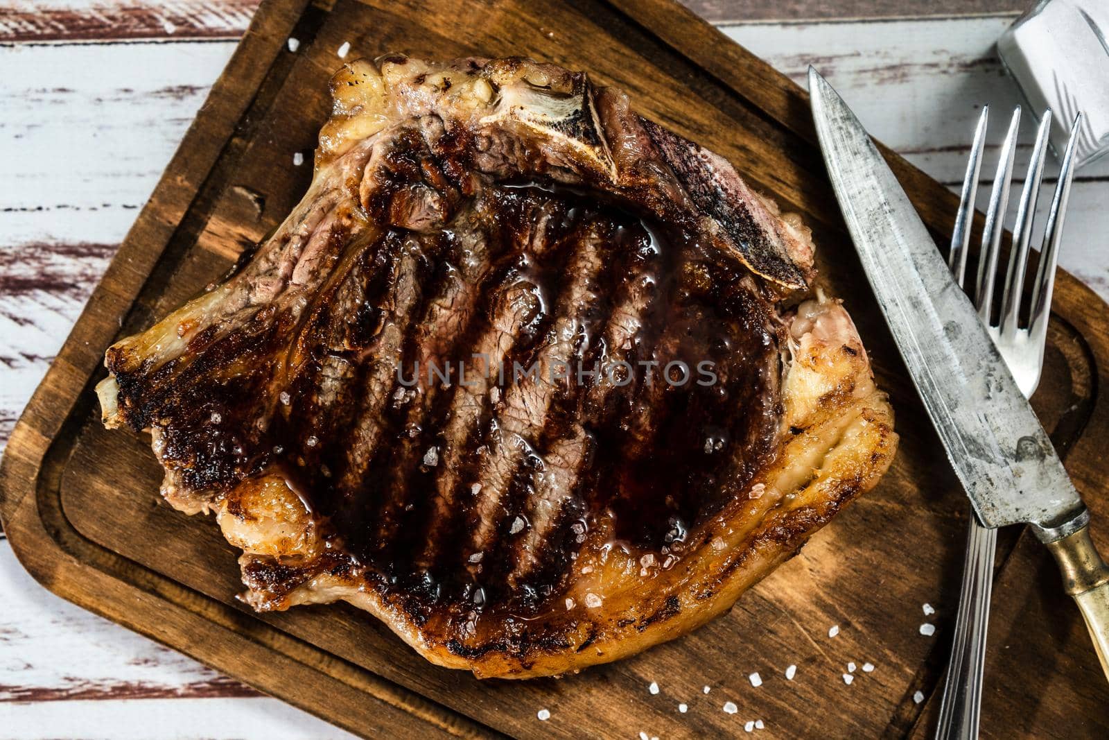 Incredible t-bone cooked on the grill or barbecue on a wooden board with cutlery on the side. Top view.