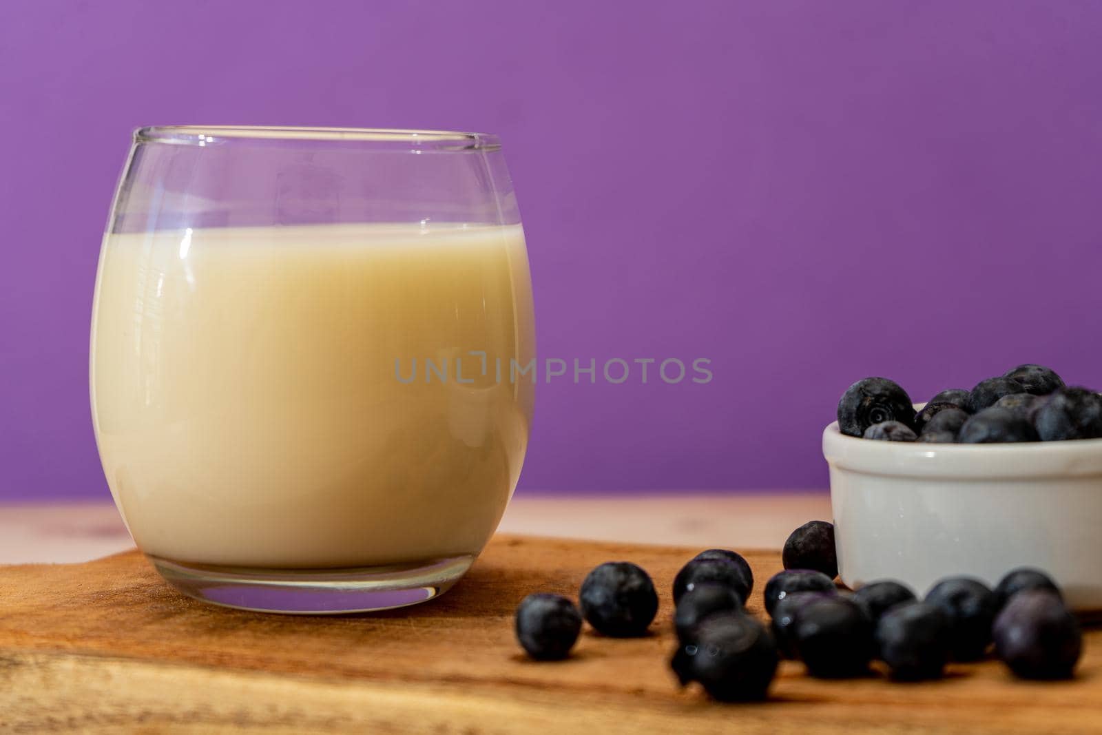 Normal view of a glass of milk next to some blueberries in a modern, stripped-down setting.