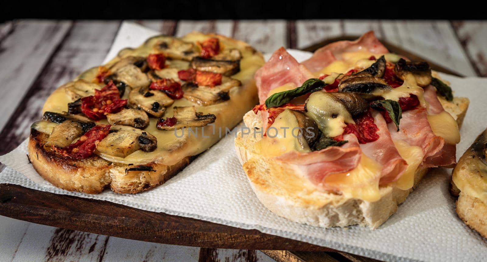 Large bruschettas with cheese, mushrooms, prosciutto and tomato in different combinations. Mediterranean food concept.