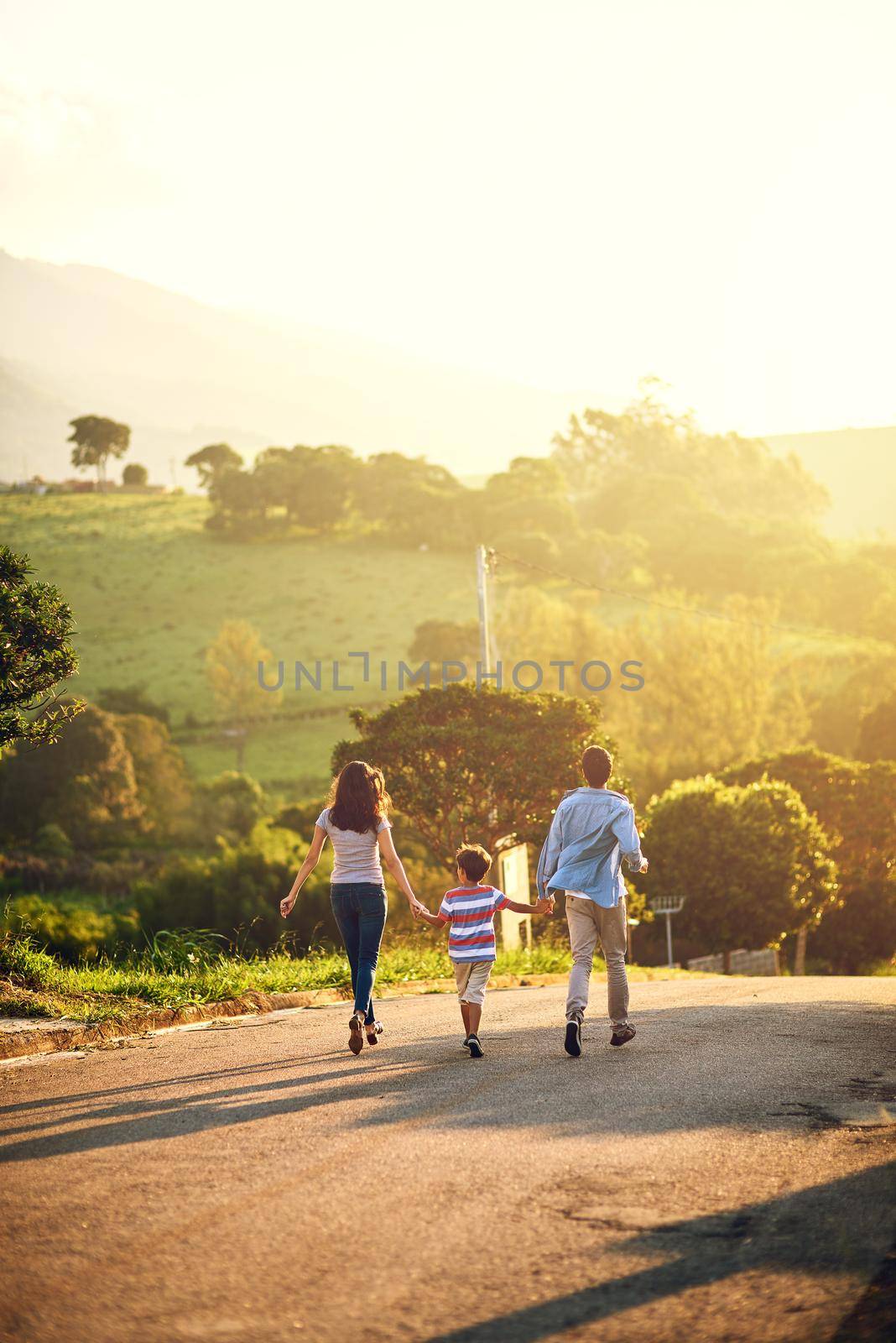 Strolling along to a leisurely day. Rearview shot of a family walking in the countryside. by YuriArcurs