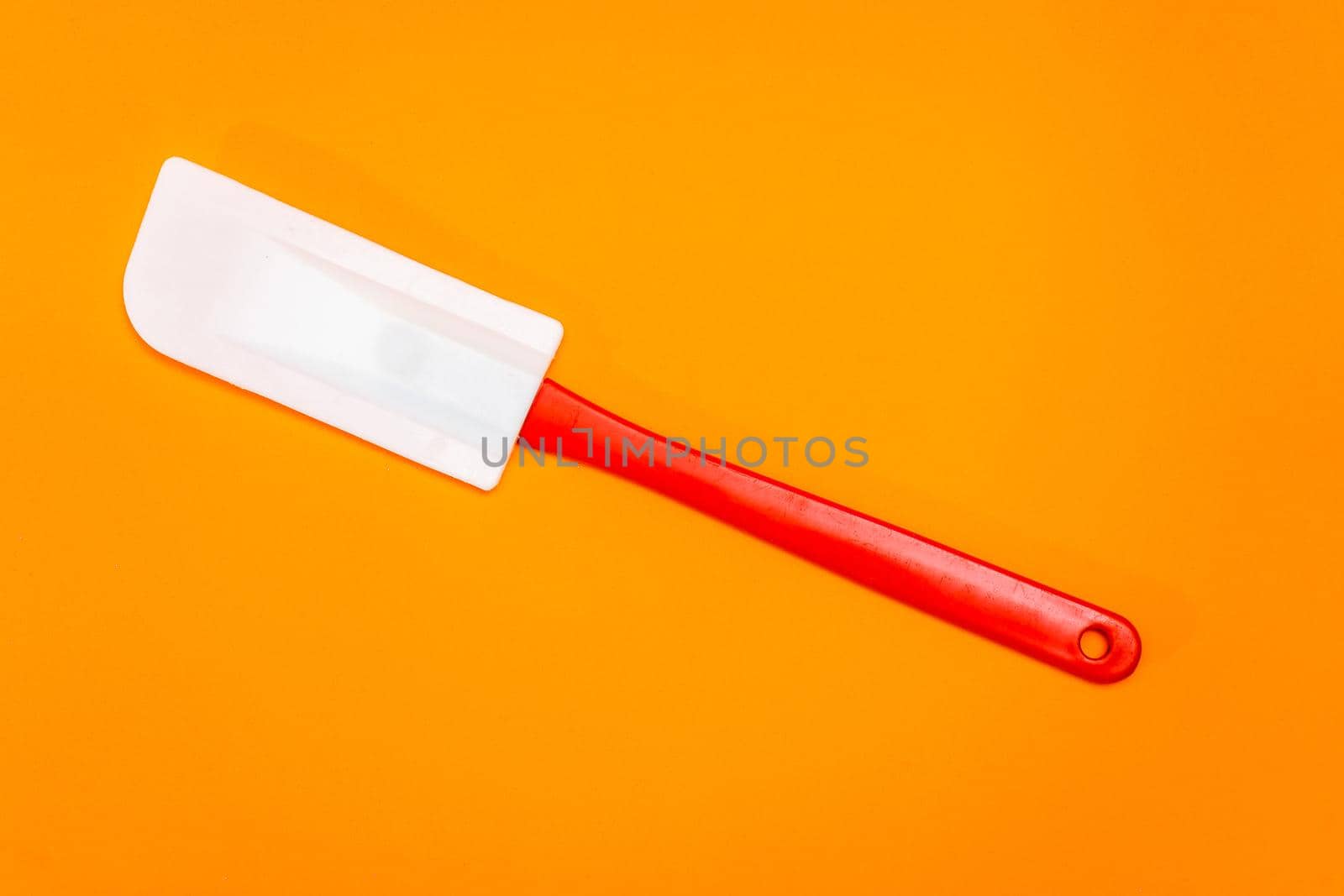 Red and white kitchen spatula made of silicone and plastic insulated on a Orange surface. Kitchen and pastry utensil.