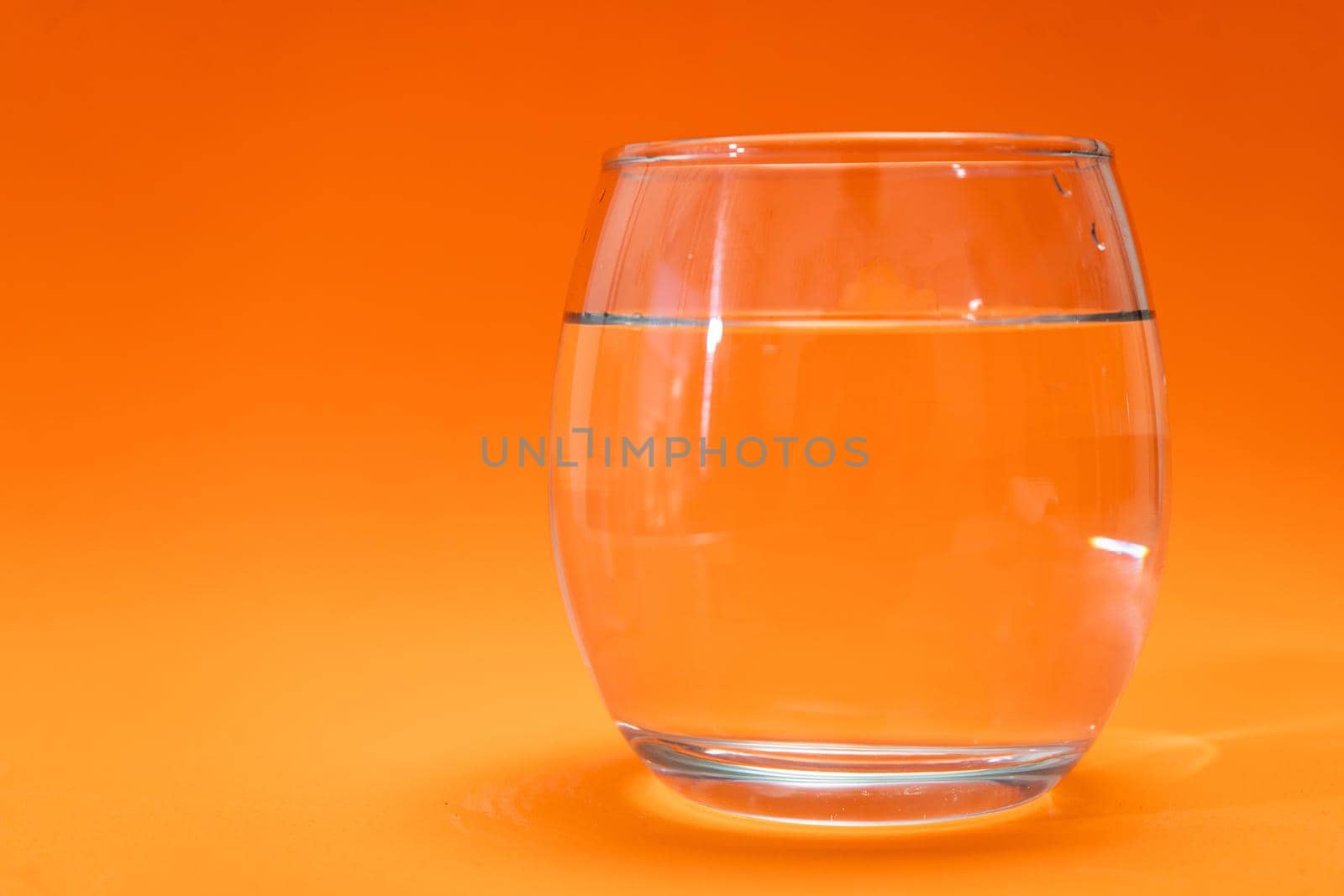 Glass tumbler with purified water on orange gradient background. Copy space