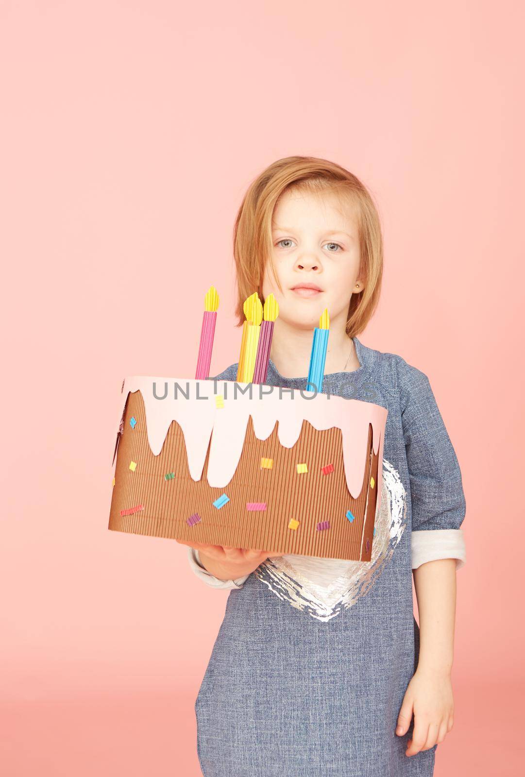 Portrait of an excited pretty little girl celebrating birthday and showing cake on over pink background.