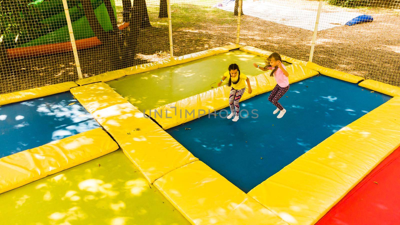 Little pretty girls having fun outdoor. Jumping on trampoline in children zone. Amusement park by Andelov13