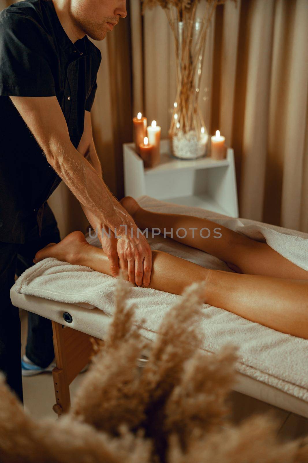 Concentrated male therapist doing professional leg massage for female client at spa center by Yaroslav_astakhov