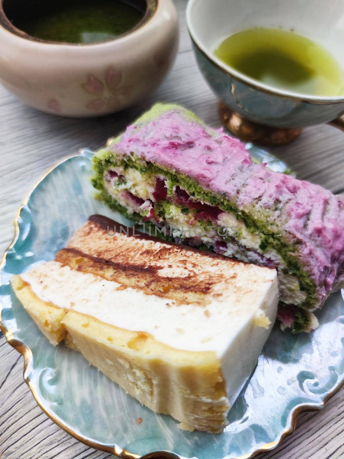 sweet fruit roll and a piece of cake on a plate, green tea in a teapot and cup, top view by Annado