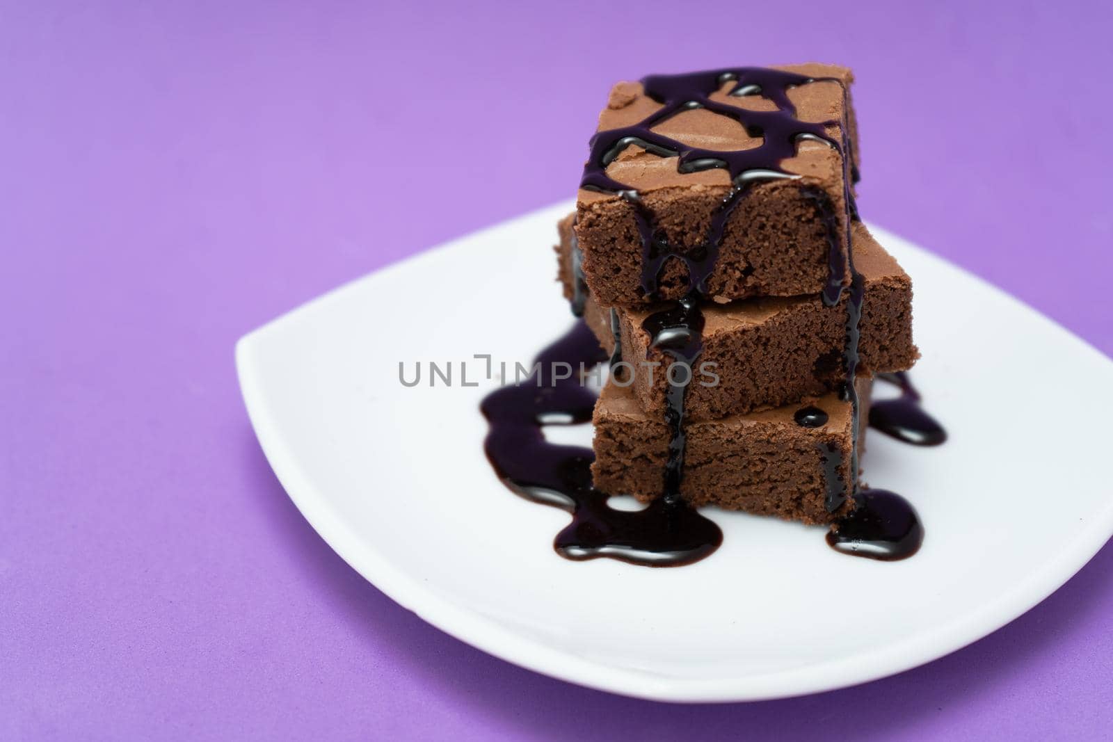 Stack of chocolate brownies on a white plate with purple background. High view.