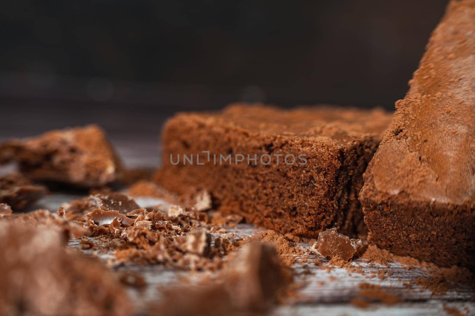 Close up of a Chocolate brownies on a rustic wooden table with chocolate chips and chocolate soil next to the brownie portions.