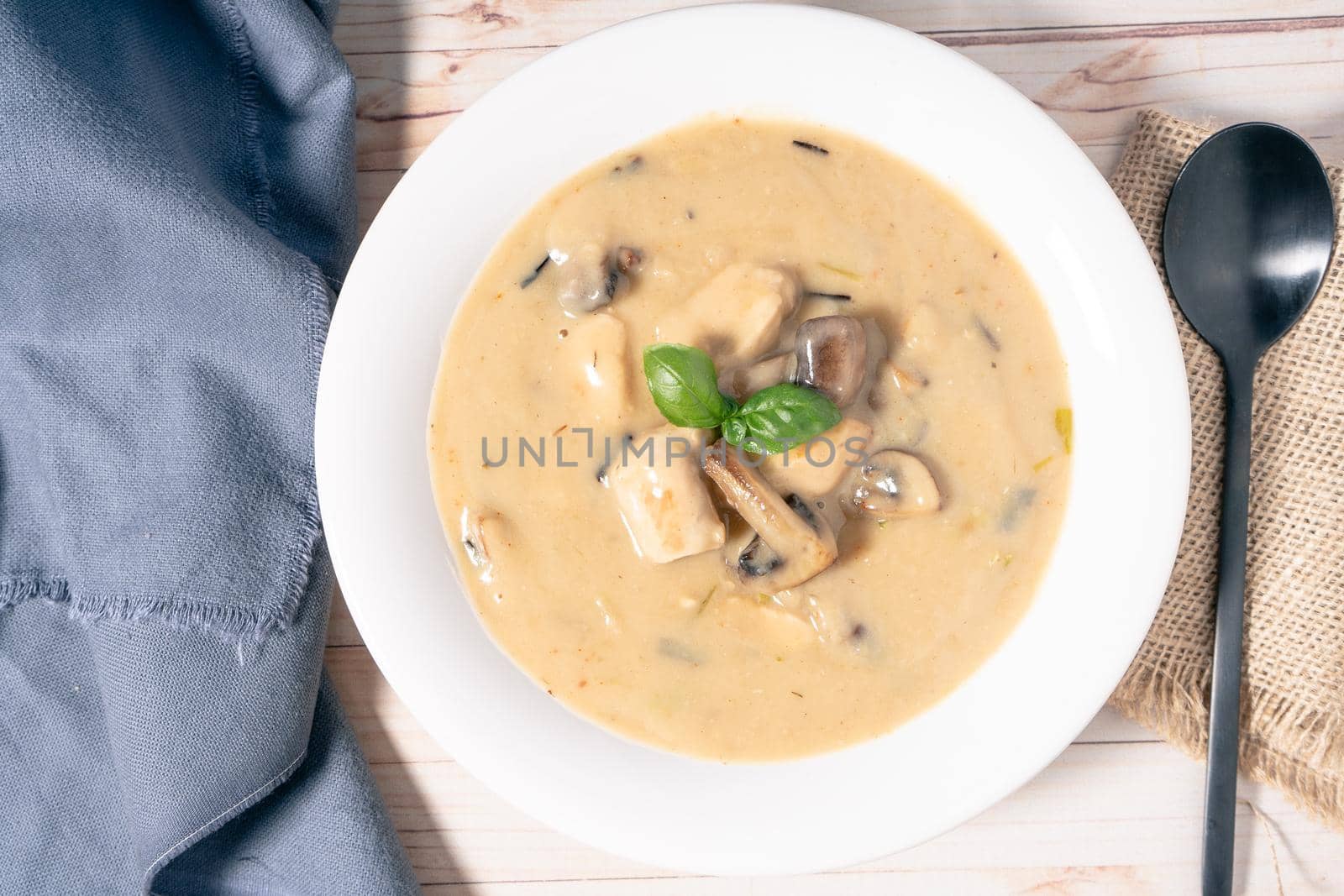 A Homemade cream of chicken and mushroom soup or French style chicken fricassee, in a white soup bowl on a wooden table. Aerial view