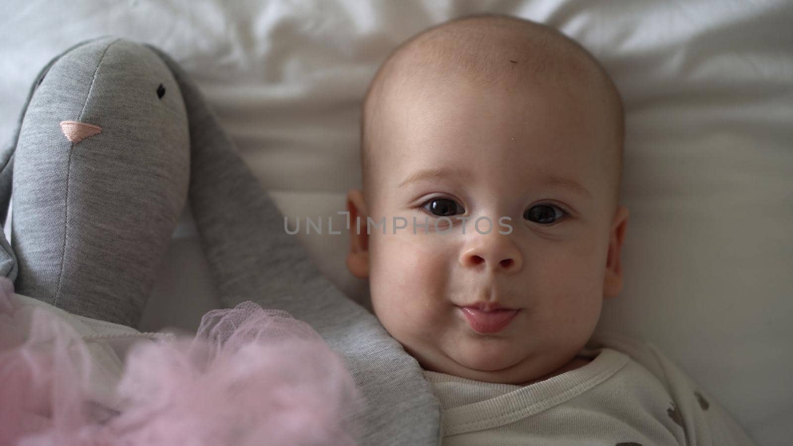 Close-up Happy playful kid 6 month old. Newborn boy looking at camera after bath shower on white soft bed. baby child waking time before bedtime with Toy. Childhood, motherhood, family, infant concept.