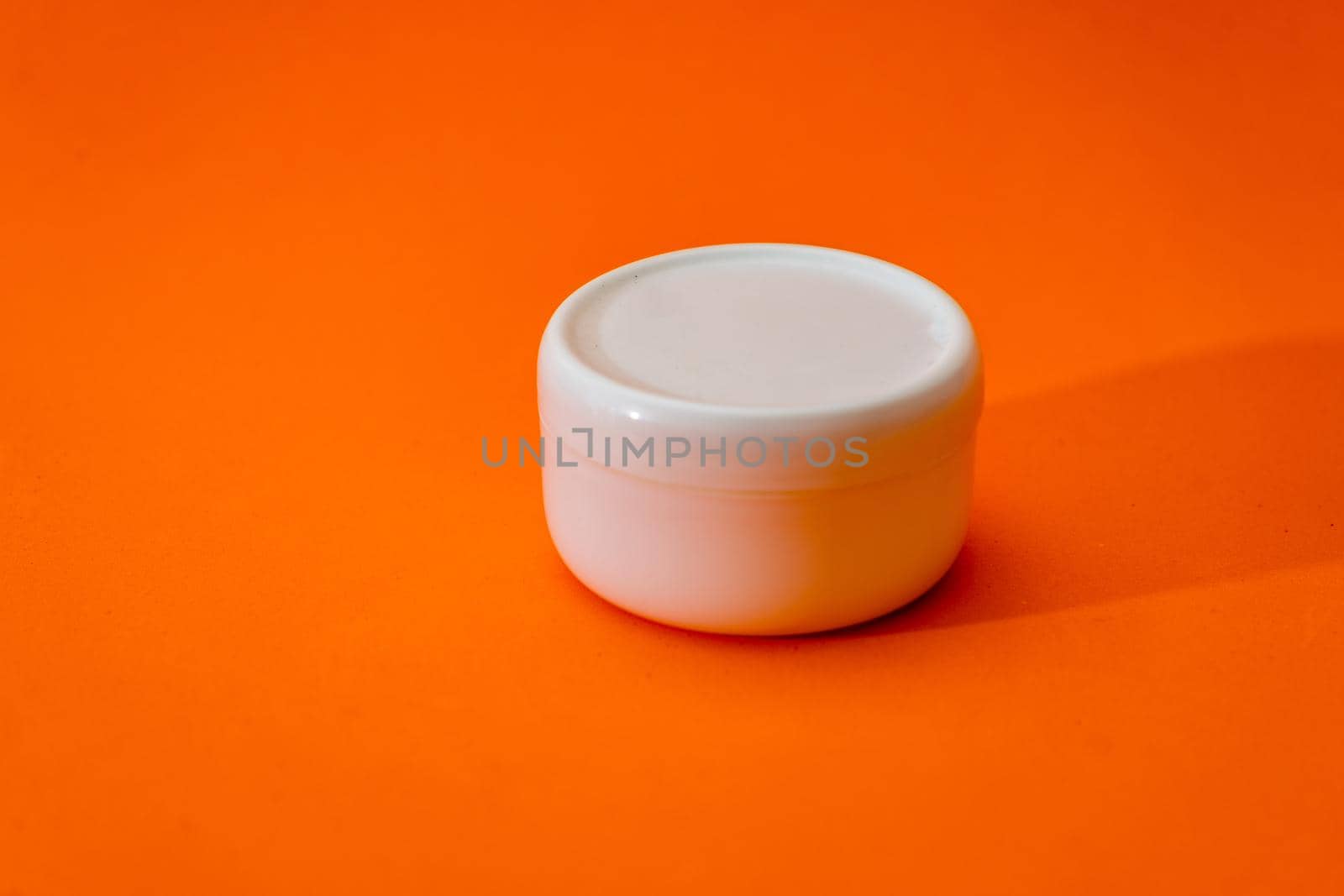 Small white plastic cream jar with lid isolated on orange background. copy space.