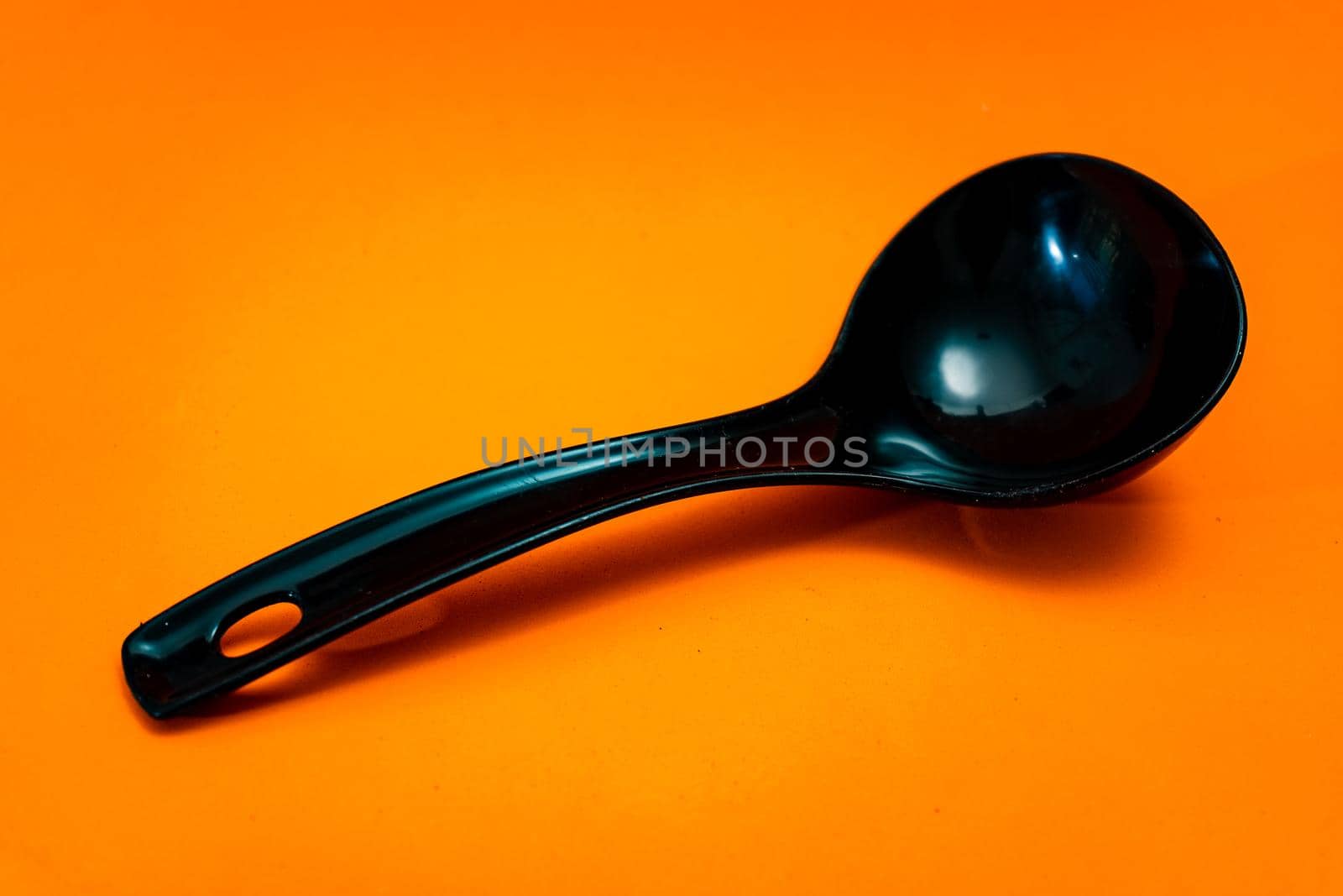 Black kitchen spoon isolated on orange background. Kitchen utensils