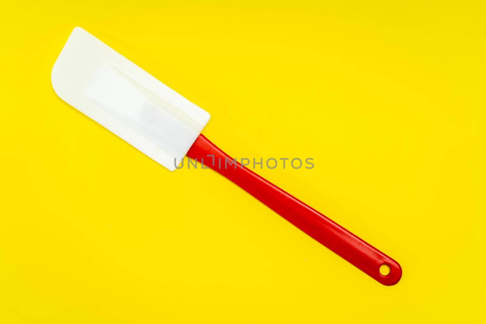 Red and white kitchen spatula made of silicone and plastic insulated on a yellow surface. Kitchen and pastry utensil.