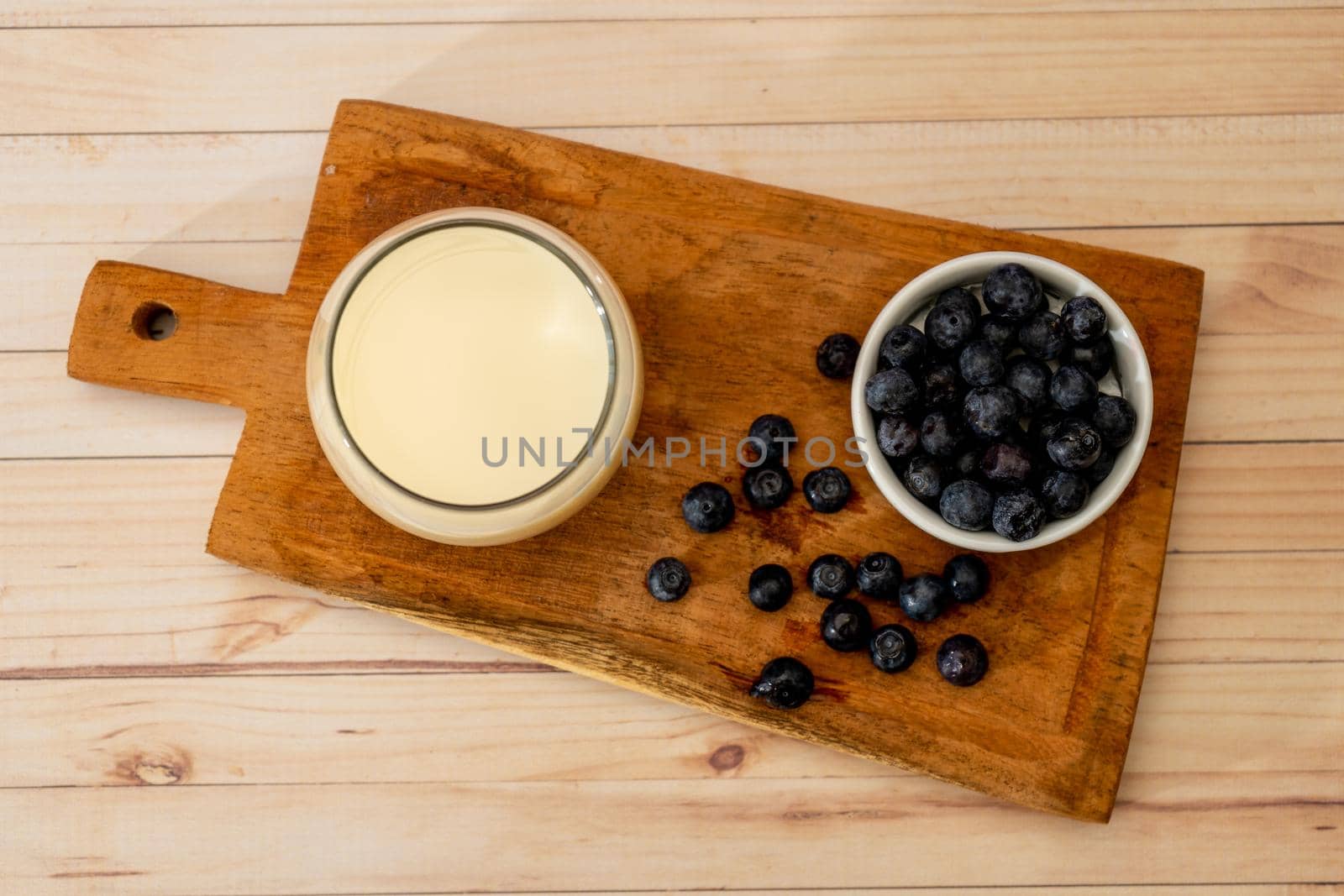 Top view of a glass of milk next to some organic blueberries on a wooden board on a table. Healthy eating
