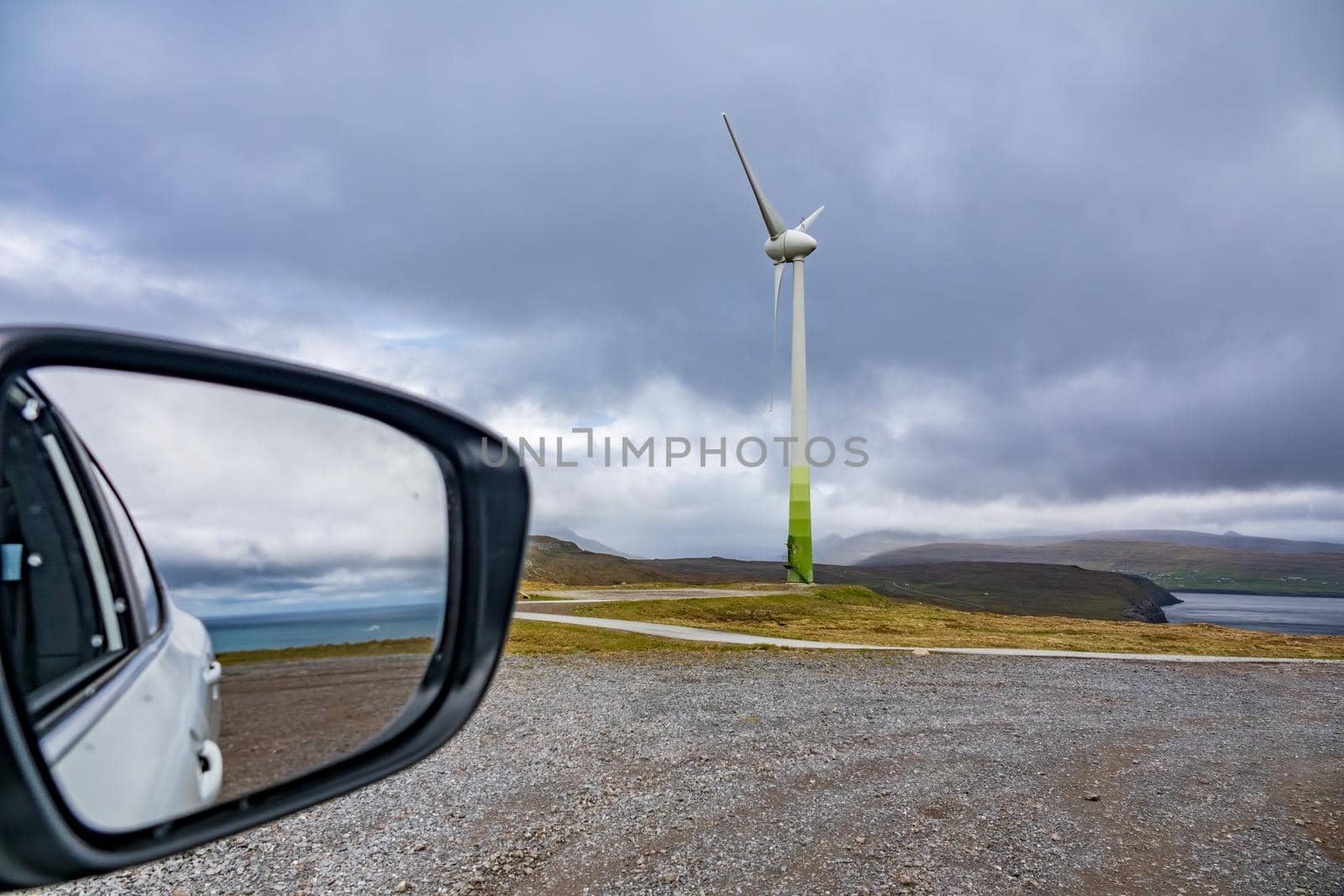 Car mirror with ocean and windmill under cloudy sky with text space