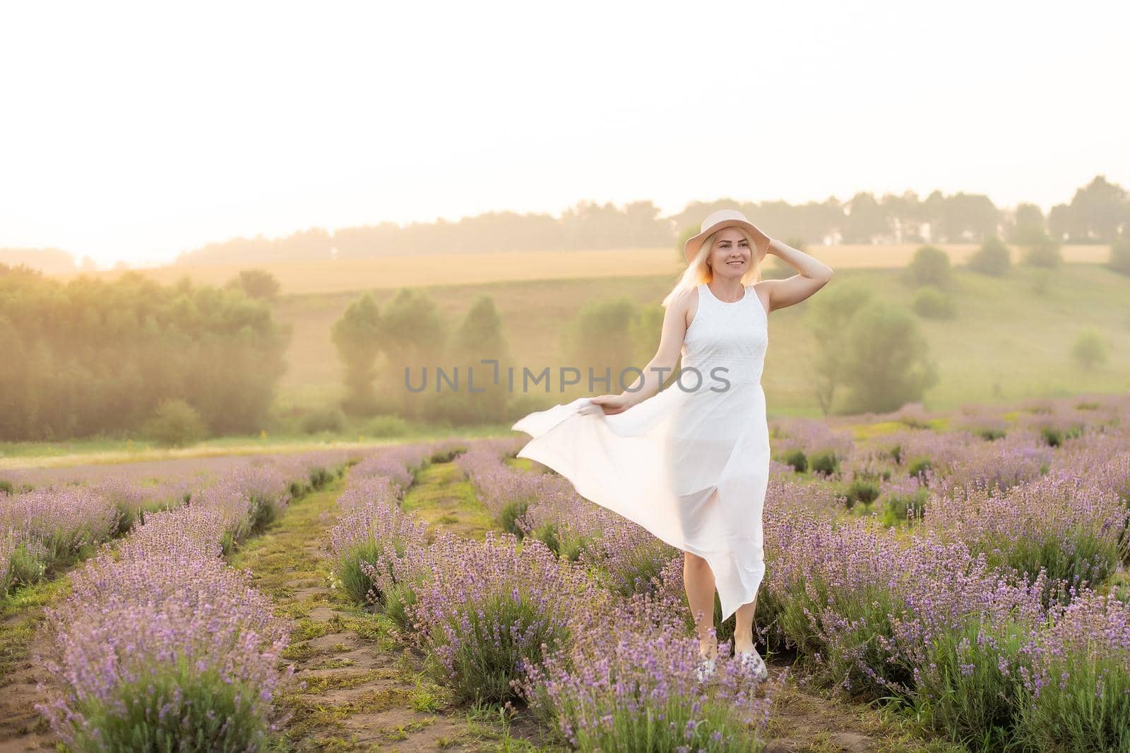Beautiful young woman walking the field of lavender. Fashion outfit dress, straw hat