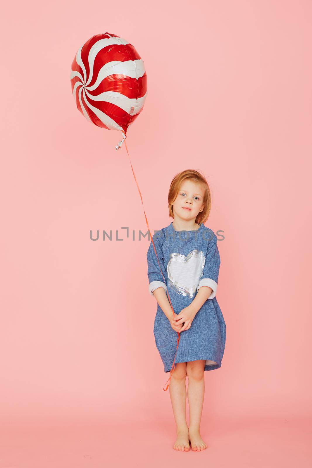 Portrait of an excited pretty little girl celebrating birthday and holding balloon in hand on over pink background