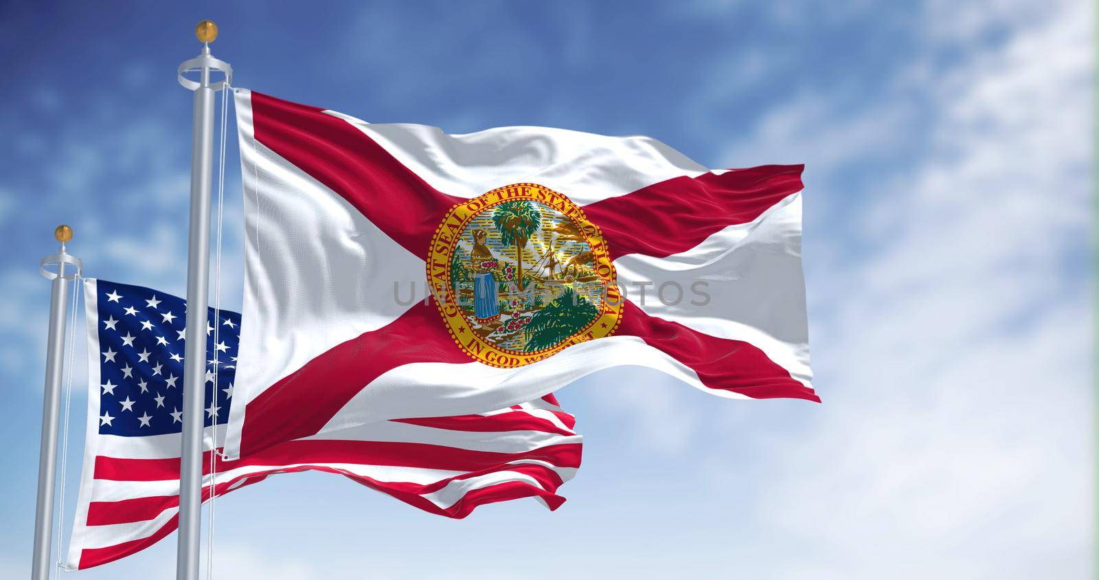 The Florida state flag waving along with the national flag of the United States of America. In the background there is a clear sky.