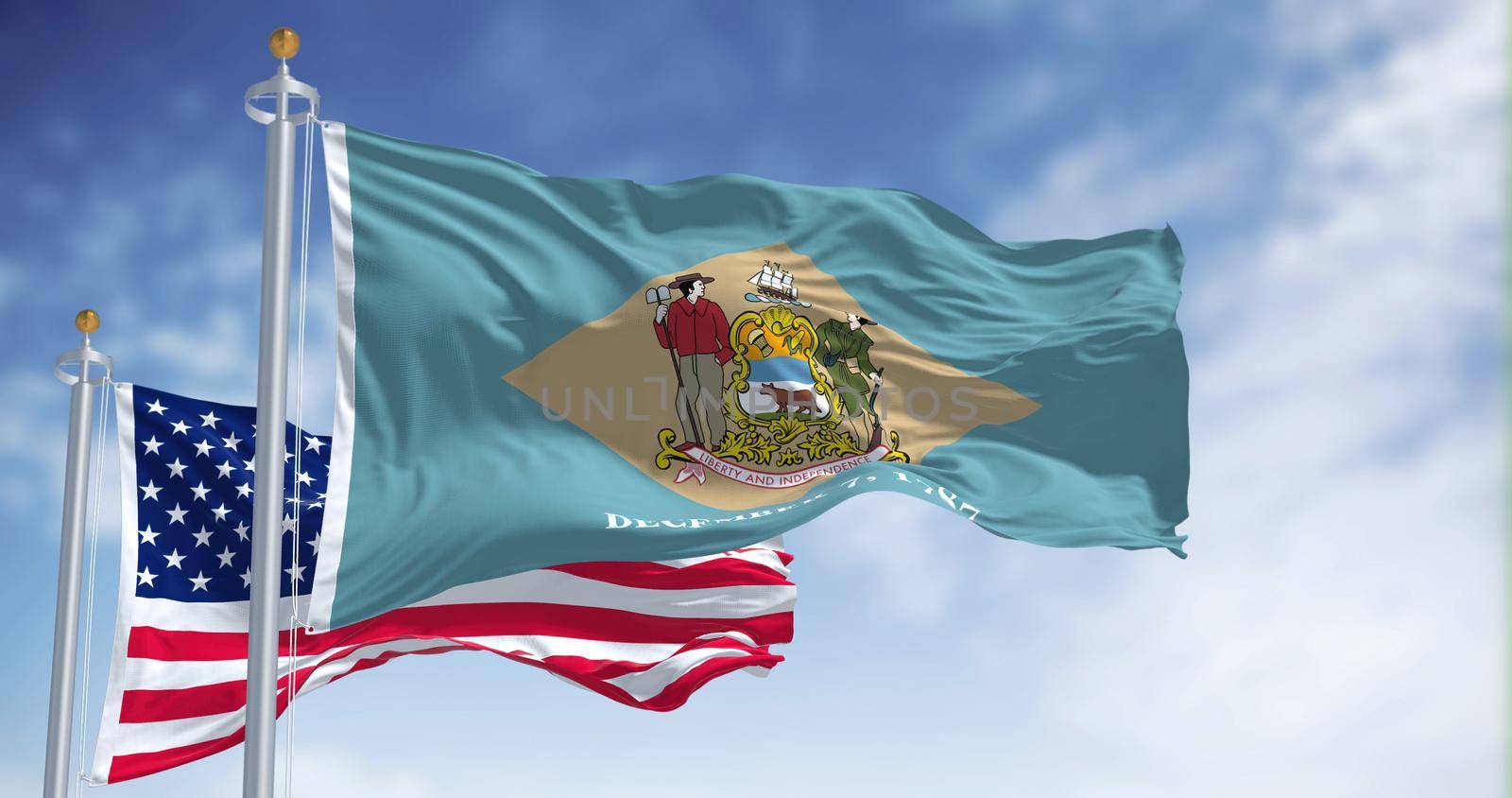 The Delaware state flag waving along with the national flag of the United States of America. In the background there is a clear sky.