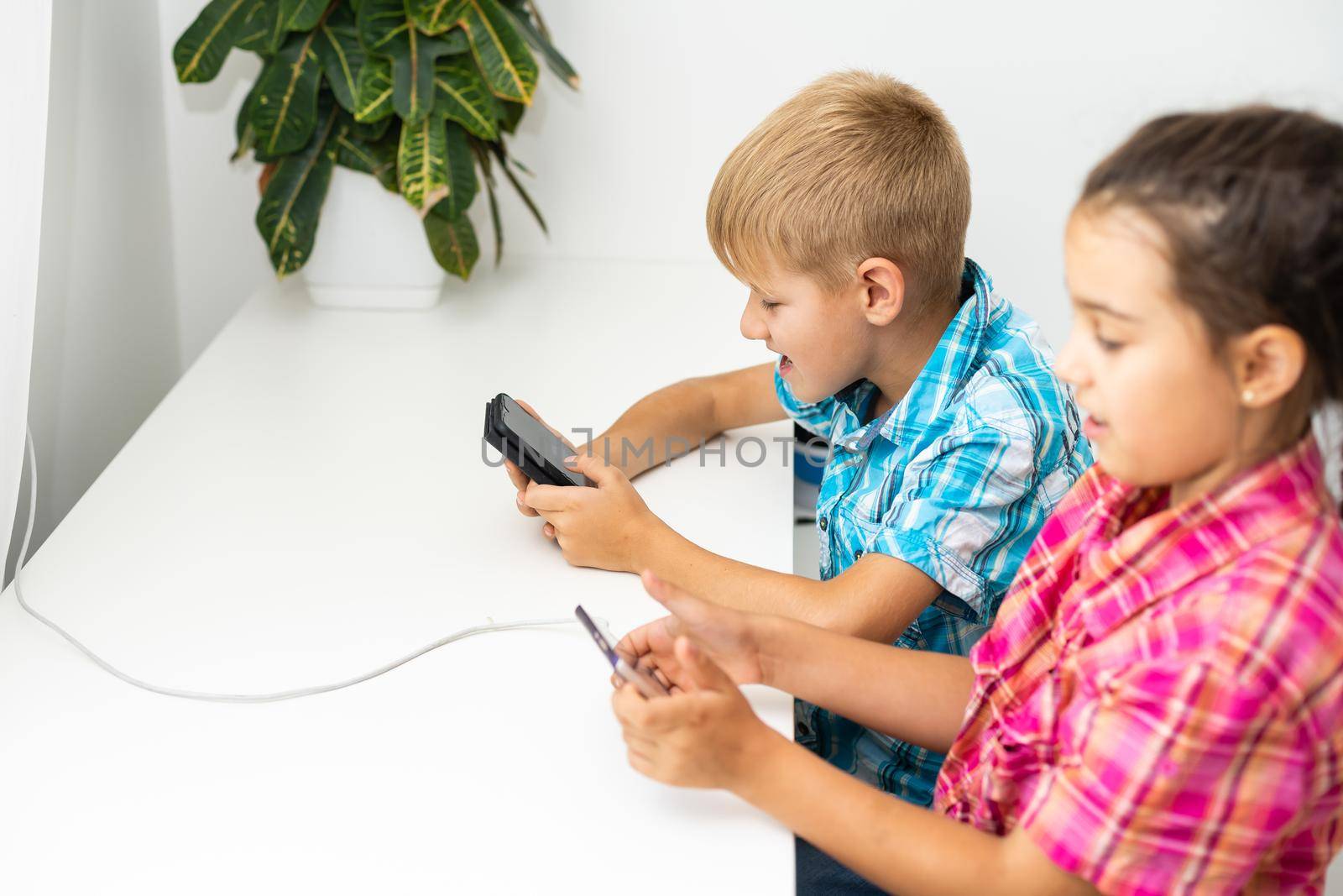 Two preschool children boy and girl sit together and play with smartphone.