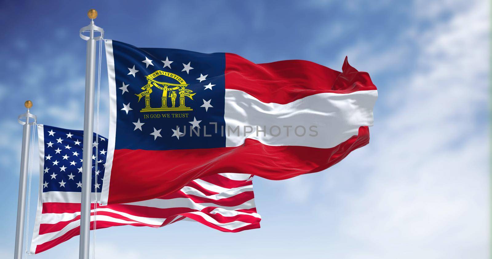 The Georgia state flag waving along with the national flag of the United States of America. In the background there is a clear sky.