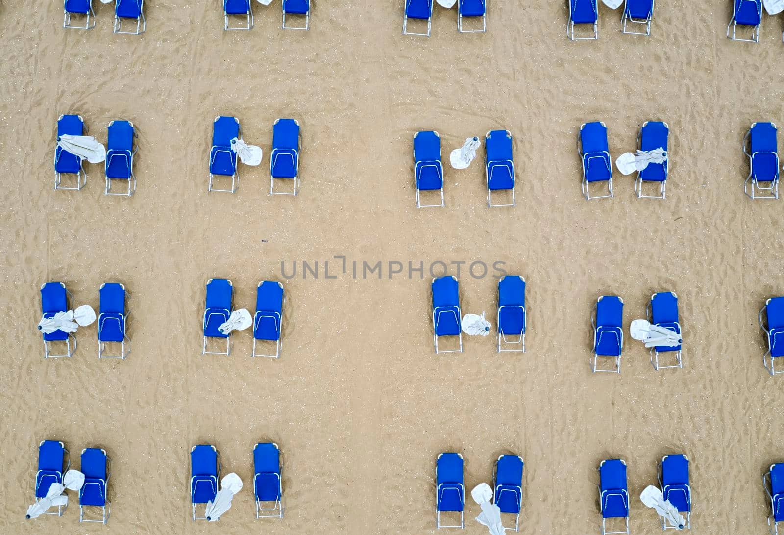 Aerial top view of a beach with white umbrellas and blue lounge chairs