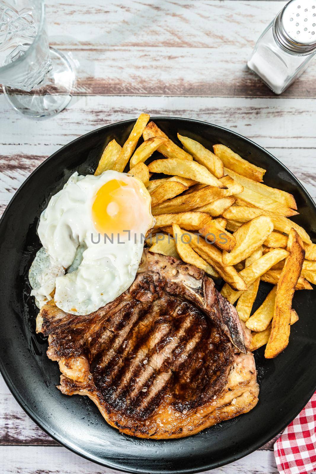 Plate with a juicy t-bone grilled or barbecued, accompanied by a portion of french fries and a fried egg. Traditional, homemade food concept. vertical orientation. by hdcaputo