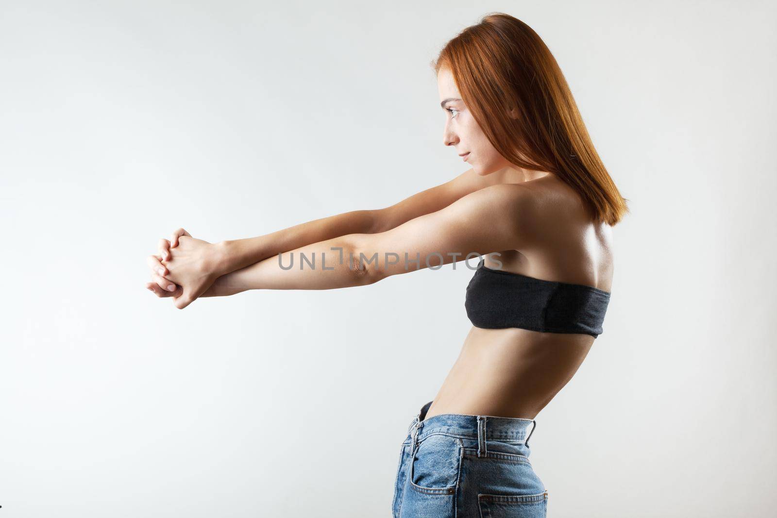 Beautiful girl with burnt orange hair stretching and making ballet pose. Studio portrait on gray background.