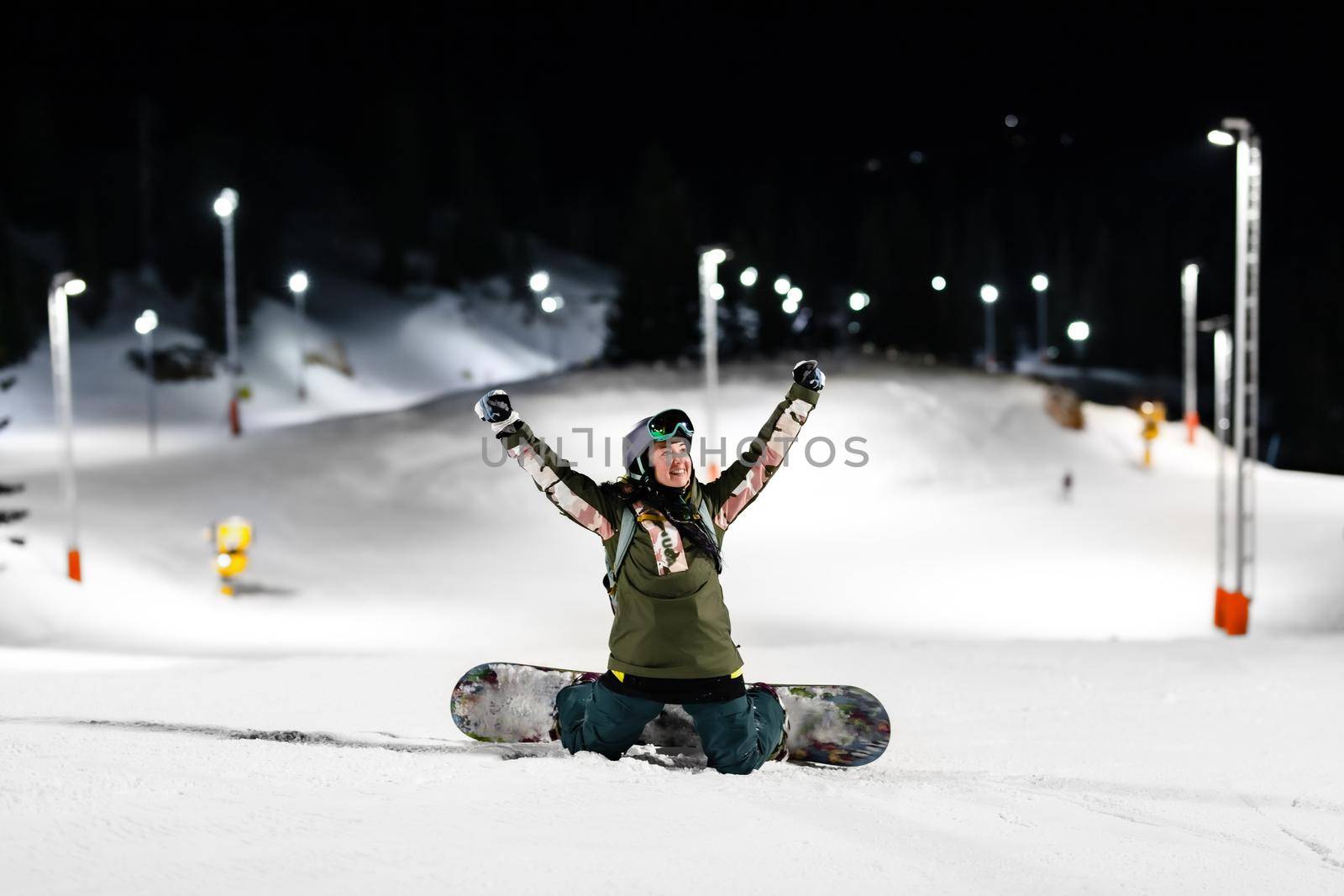 Snowboarder girl posing on slopes. Night skiing in winter resort.