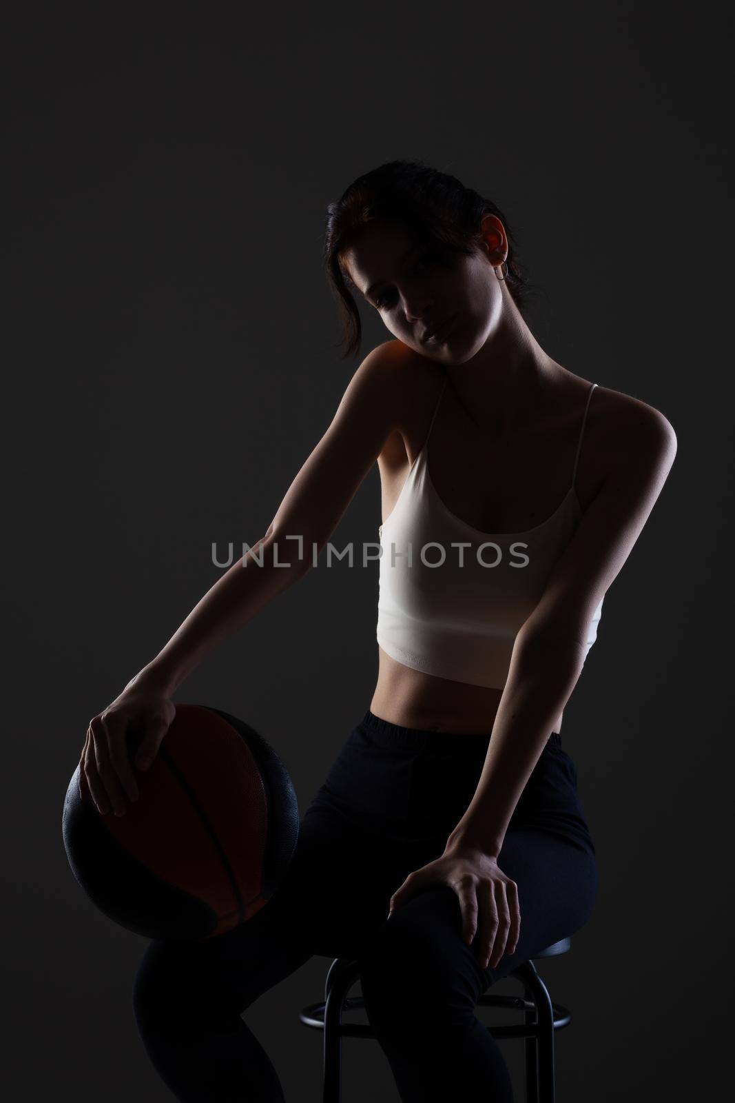 Teenage girl with basketball. Side lit studio portrait against dark background.. by kokimk