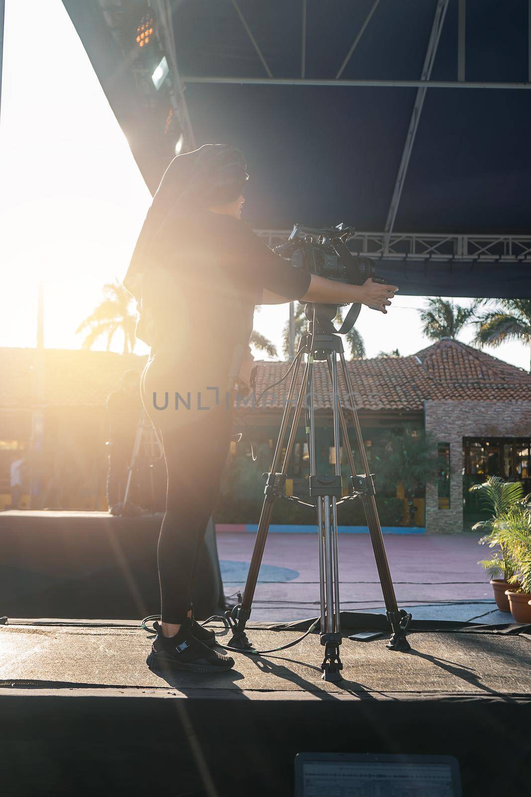 Vertical photo of an unrecognizable woman cameraman films a live tv show outdoors. A female professional as a symbol of empowerment and diversity in professions considered difficult