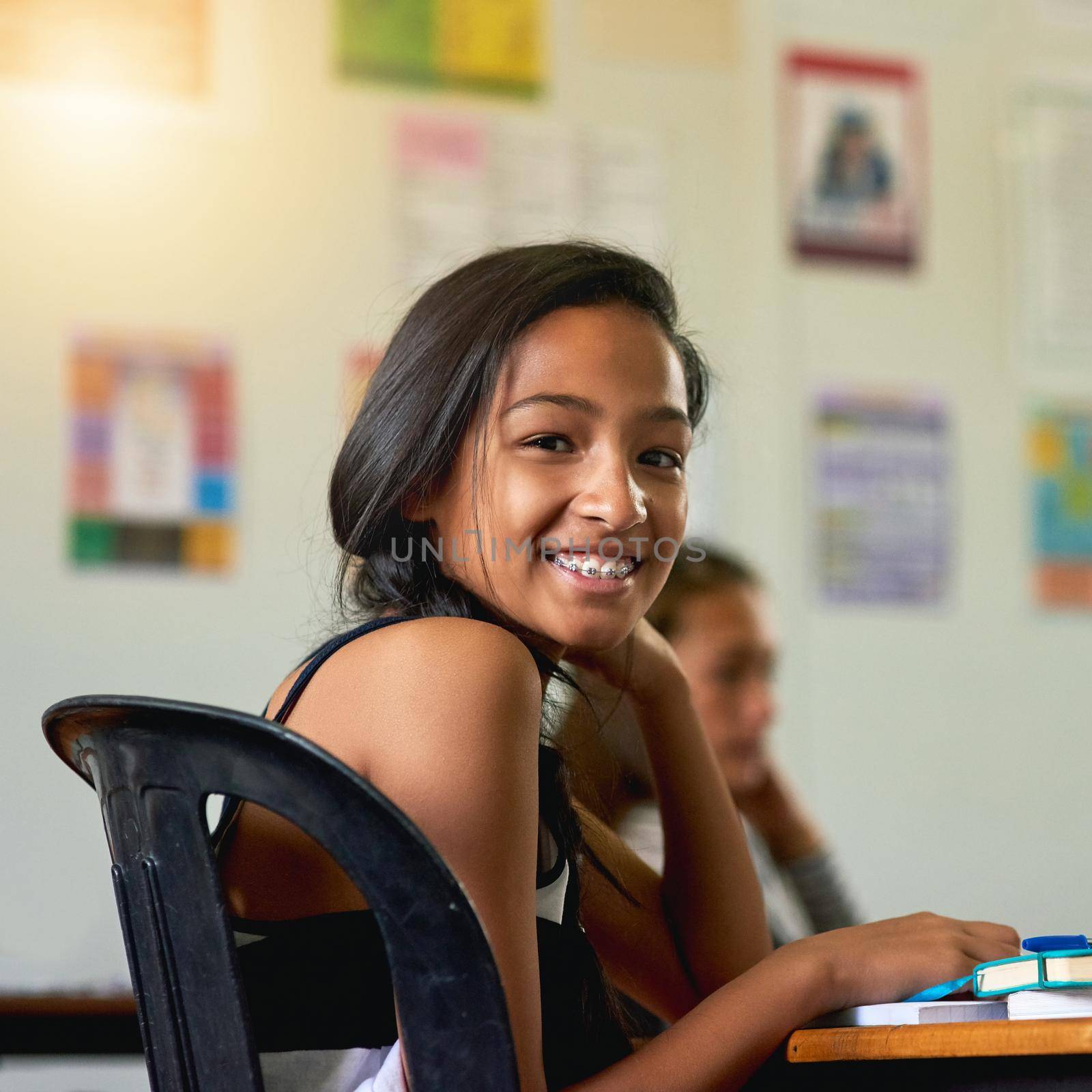 This school is super cool. Portrait of a happy young schoolgirl looking over her shoulder in class. by YuriArcurs