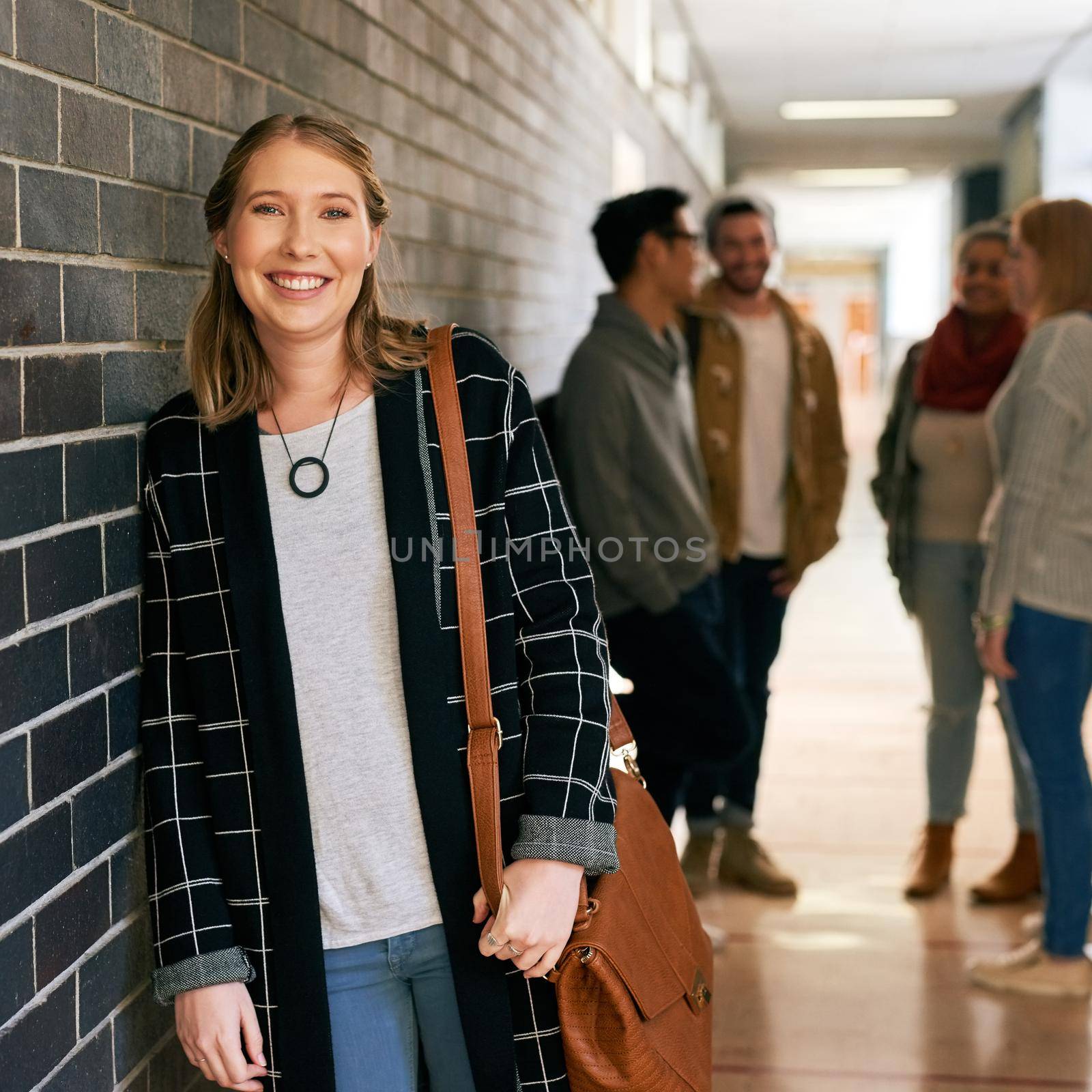 Portrait of a young female university student standing in a campus corridor with her classmates in the background.