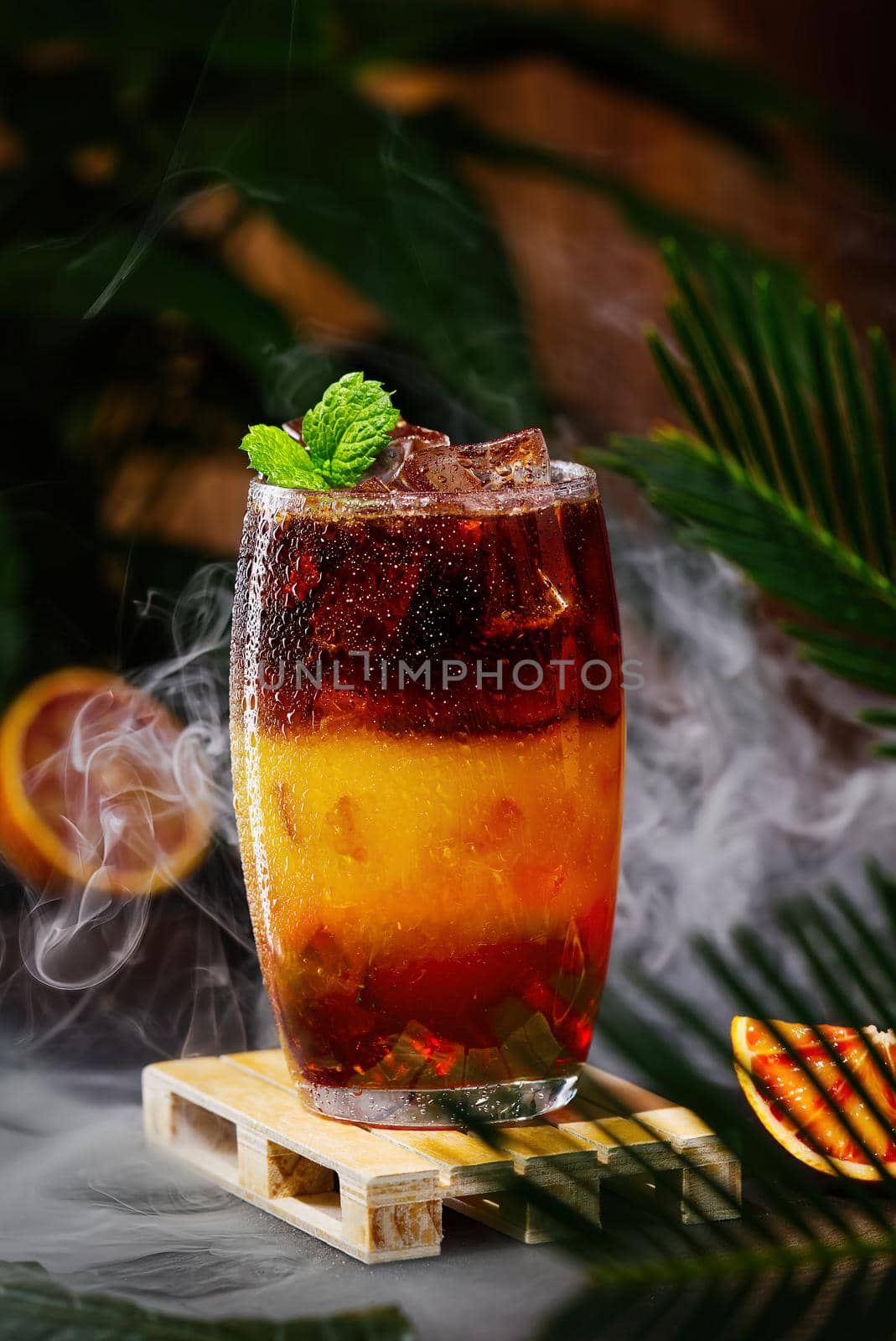 Bumble coffee with ice on a dark tropical background. Espresso, orange juice and syrup in layers in transparent glass with ice. Summer trendy refreshing coffee drink. Coffee house menu, recipe. Copy space