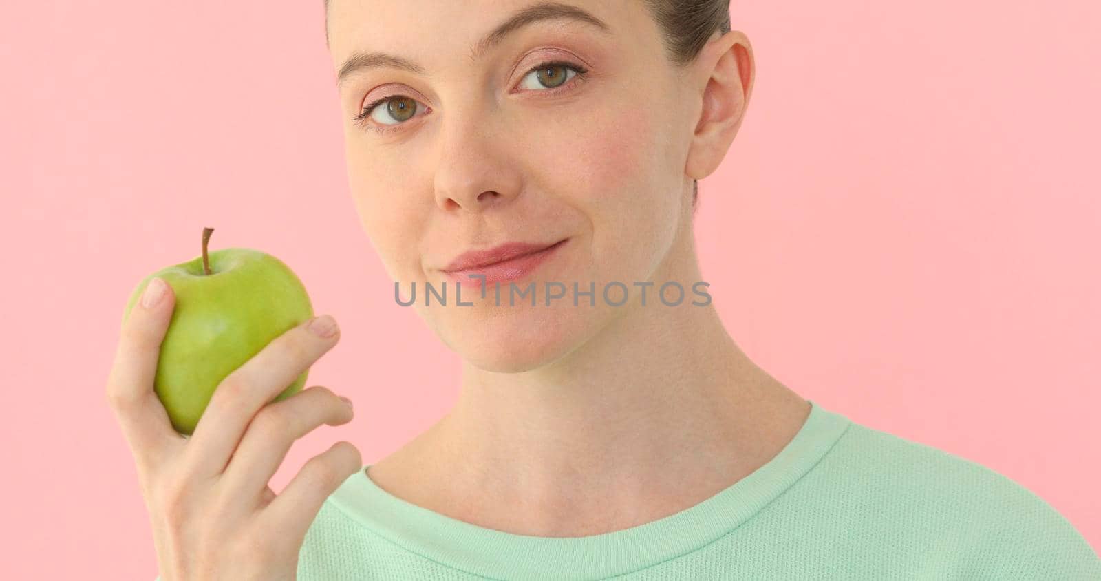 Woman enjoying fresh apple at pink background. Girl looking at camera