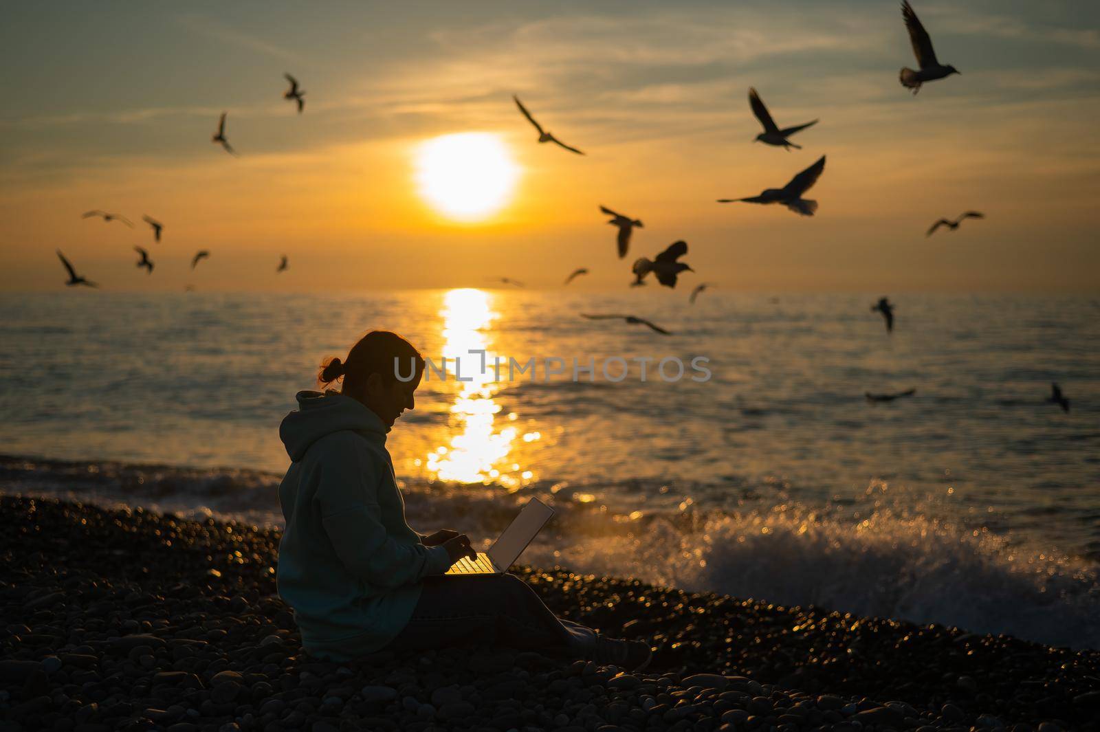 Caucasian woman typing on a laptop on the seashore at sunset. Freelance work