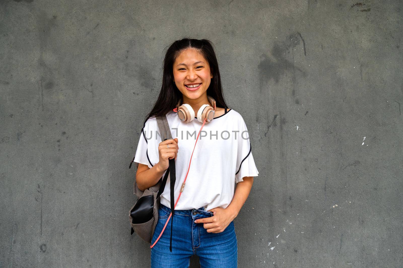 Smiling teen Asian high school student girl standing outdoors looking at camera. by Hoverstock