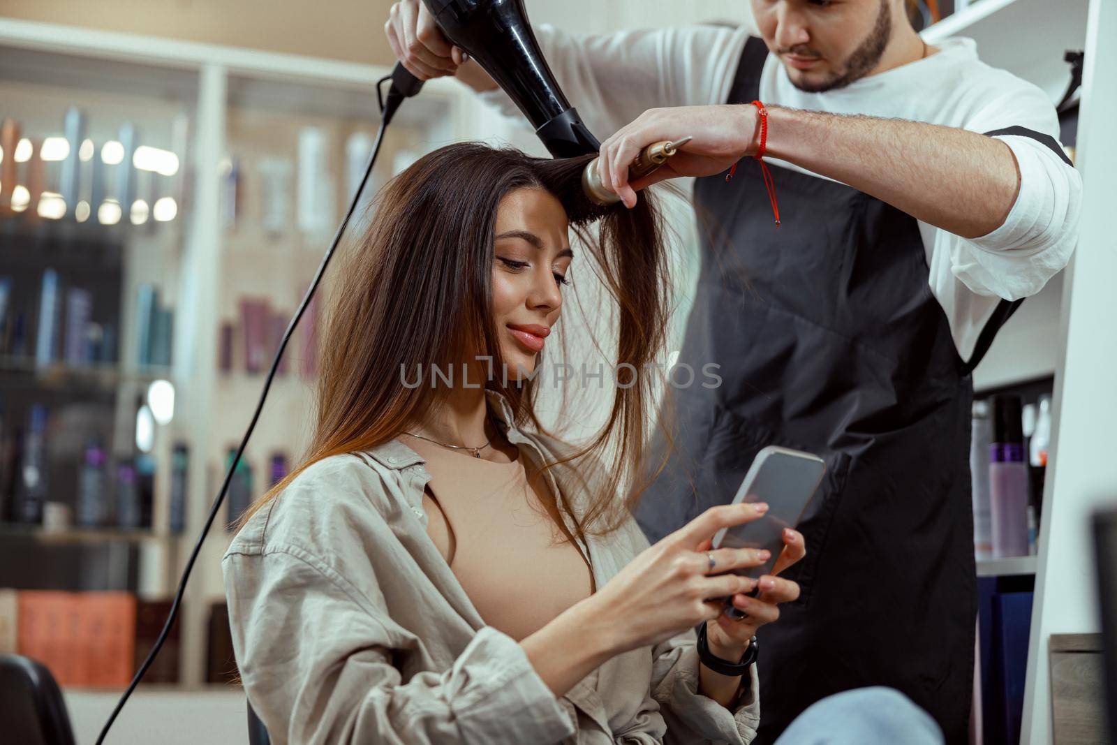 Beautiful woman with long hair using smart phone at beauty salon by Yaroslav_astakhov