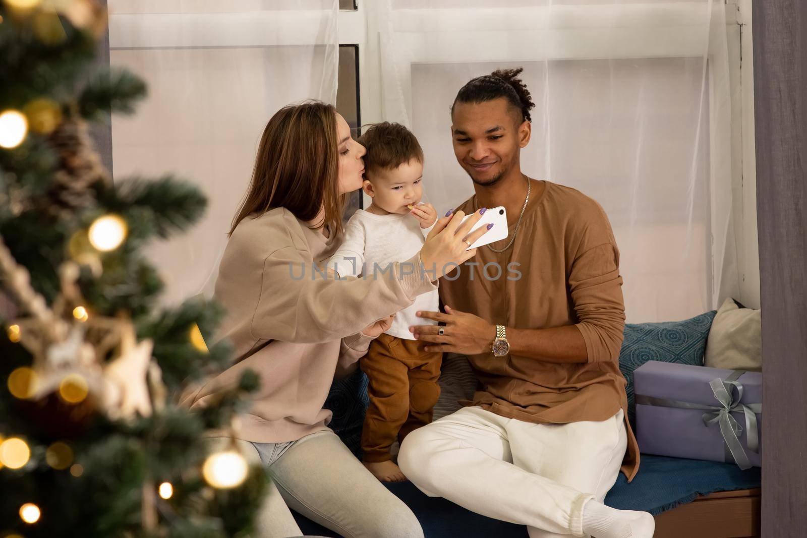 Happy young woman in cozy sweatshirts, a small son, a stylish man, sitting at home, taking a photo on a smartphone