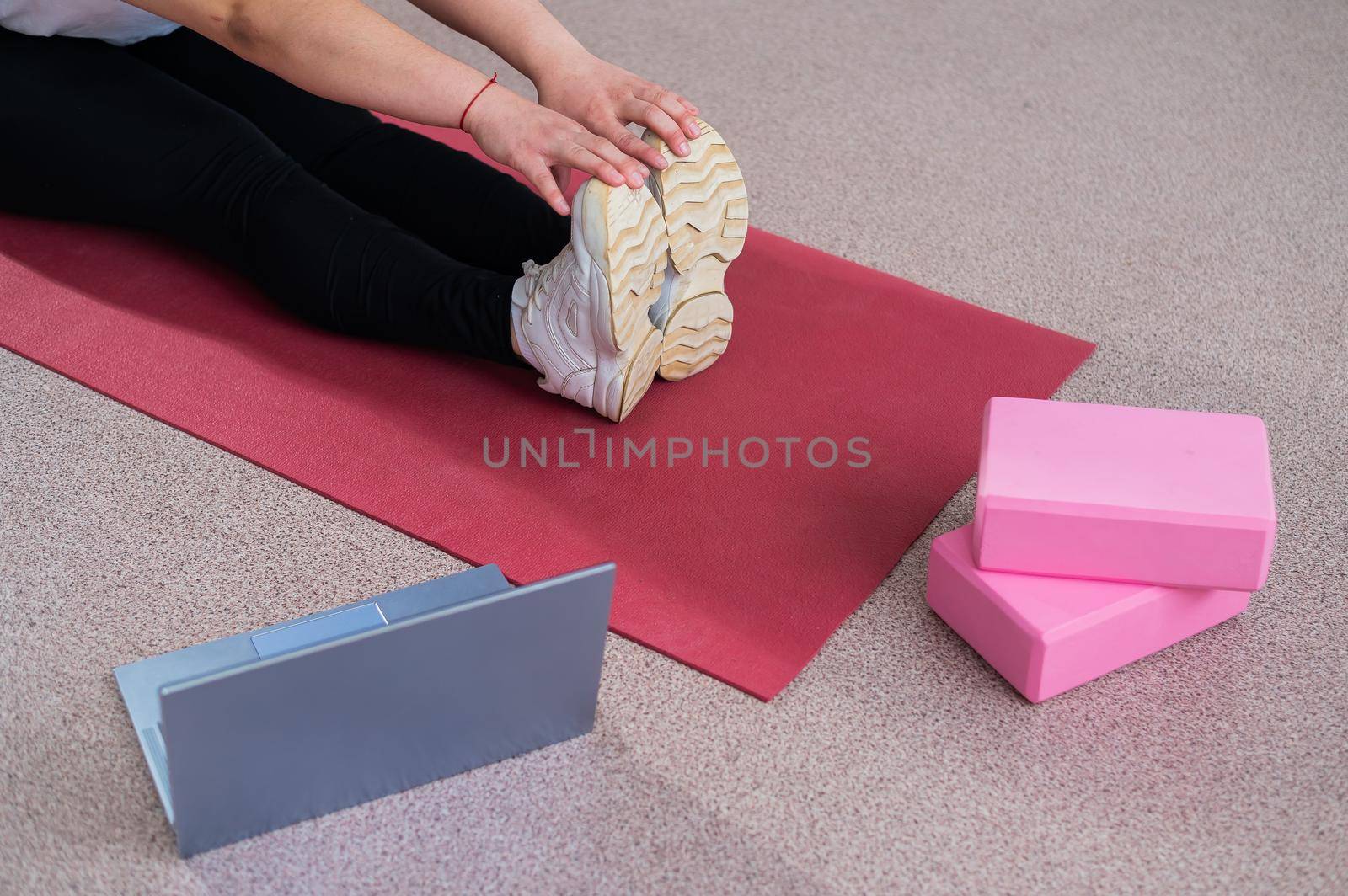 A faceless woman is watching an online yoga lesson on a laptop. Distance sports training.