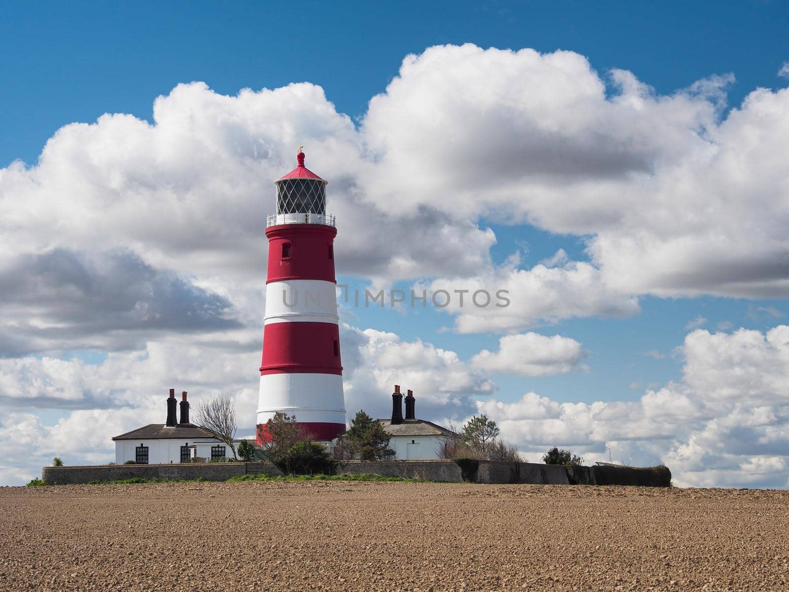 Red and white striped Happisburgh Lighthouse under blue sky and white billowing clouds, Norfolk, UK