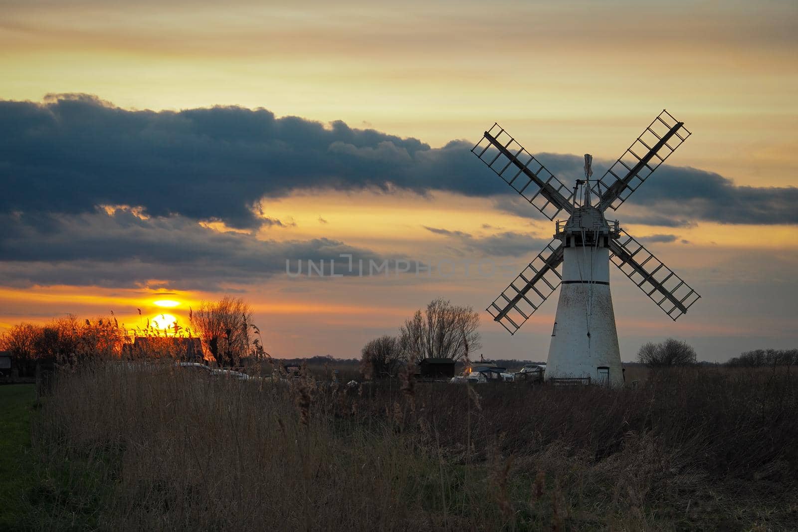 Beautiful orange sunset lighting up the clouds over Thurne Dyke Drainage Mill set in The Broads, near Great, Yarmouth, Norfolk, UK