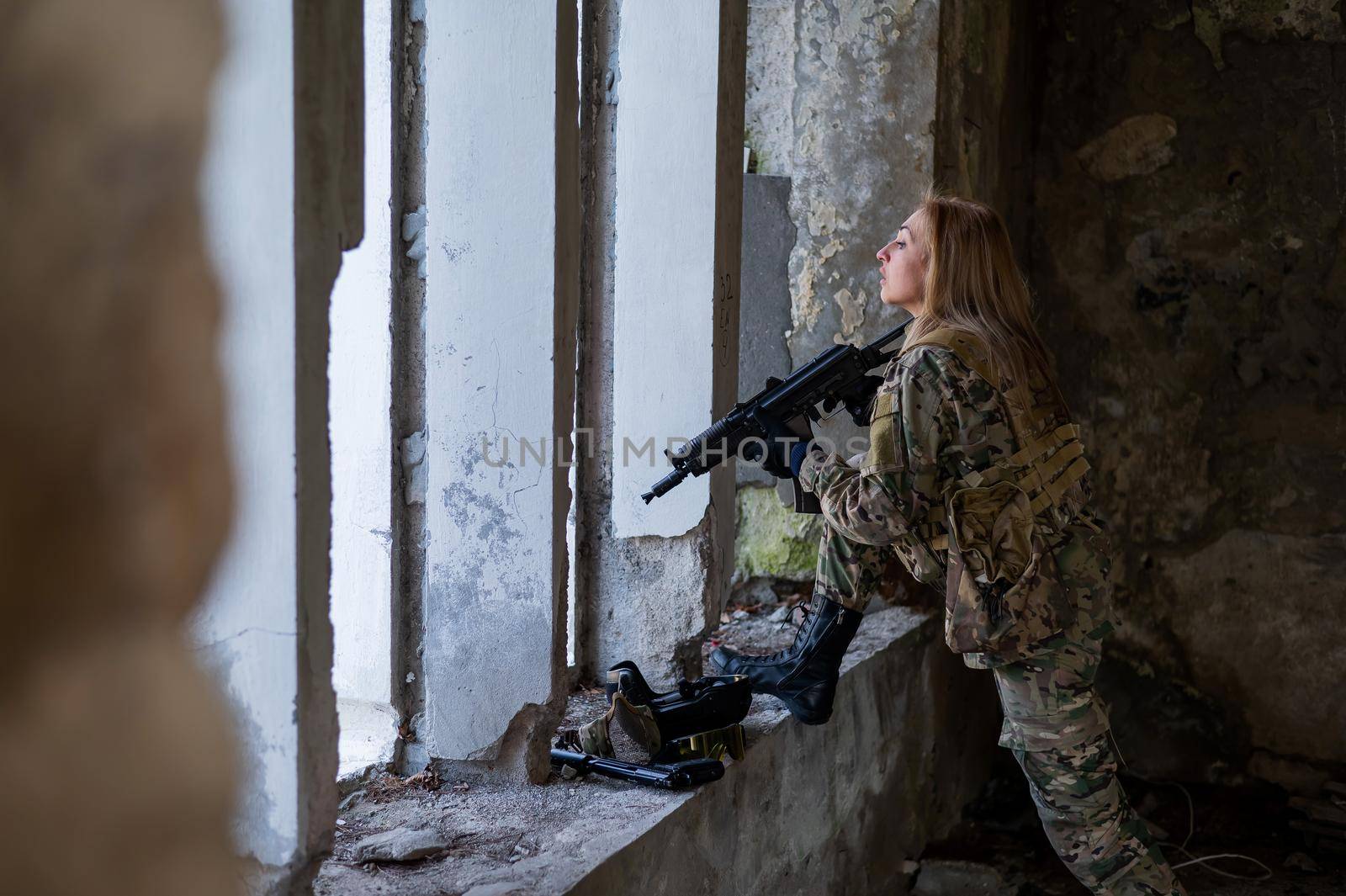 A woman in an army uniform aims to shoot a firearm in an abandoned building