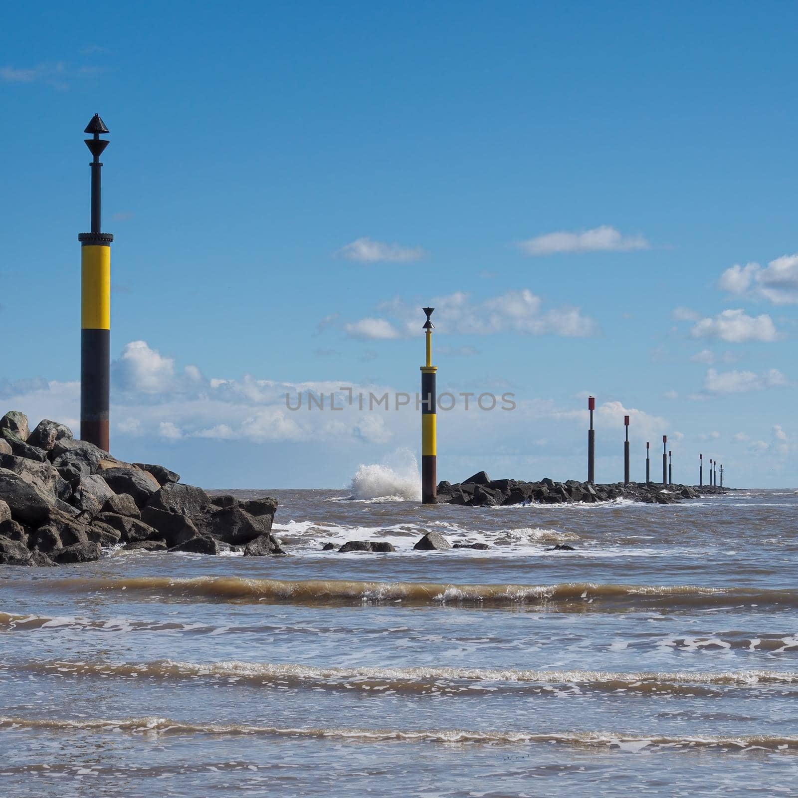 Waves crashing against the rocky breakwater with black and yellow cardinal posts marking the safe entrance to the bay, Sea Palling, Norfolk, UK