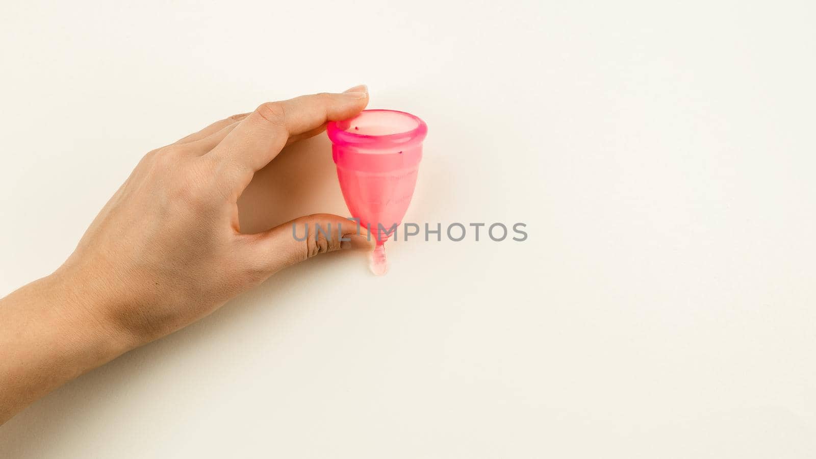 Woman hand holding a pink menstrual cup by Syvanych