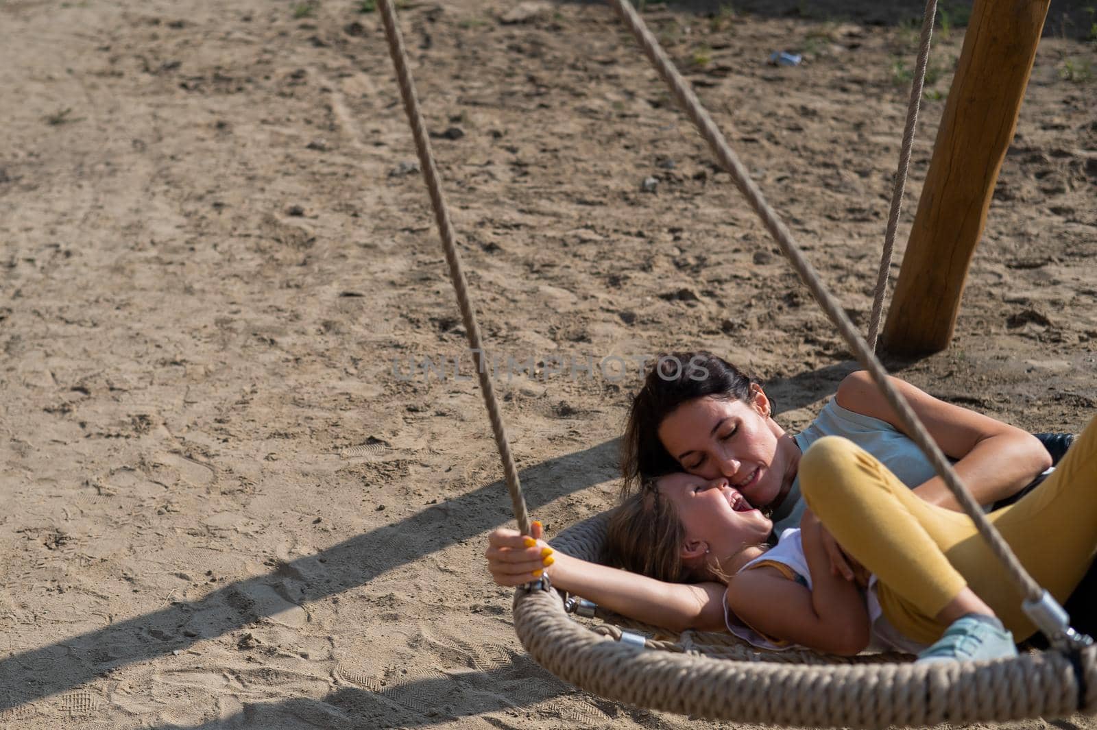 Mom and daughter swing on a round swing. Caucasian woman and little girl have fun on the playground. by mrwed54